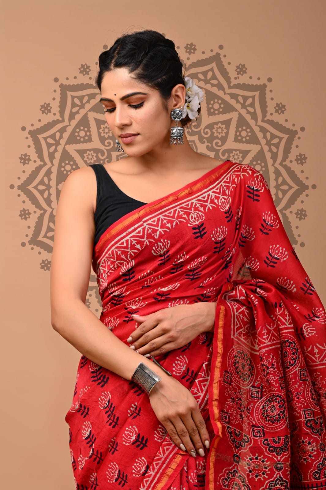Woman wearing a red saree with black patterns against a beige background